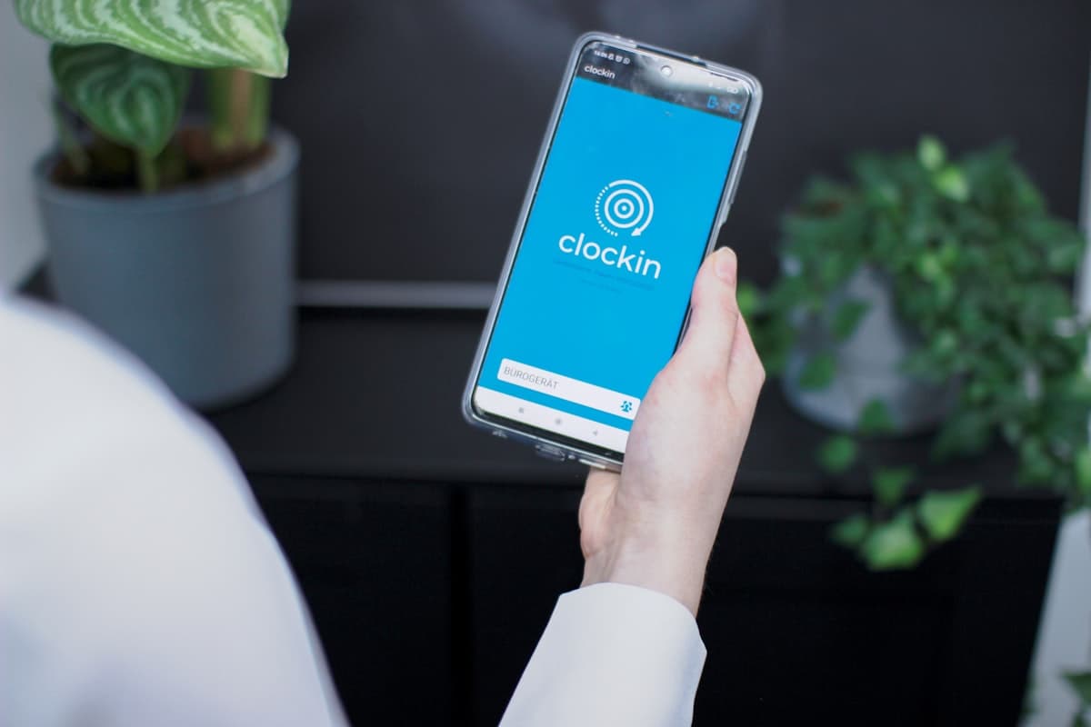 A hand holding a smartphone displaying a mobile attendance check-in app