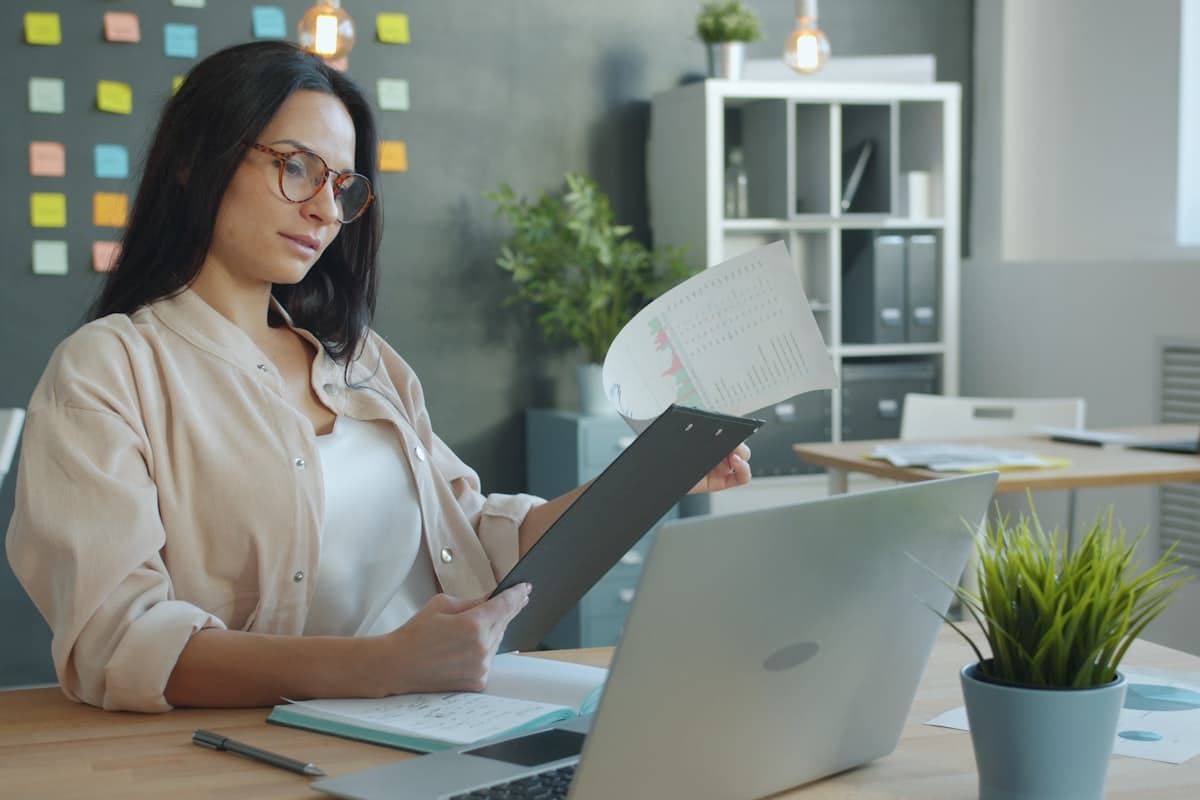 An HR professional reviewing an attendance report on a clipboard next to an open laptop