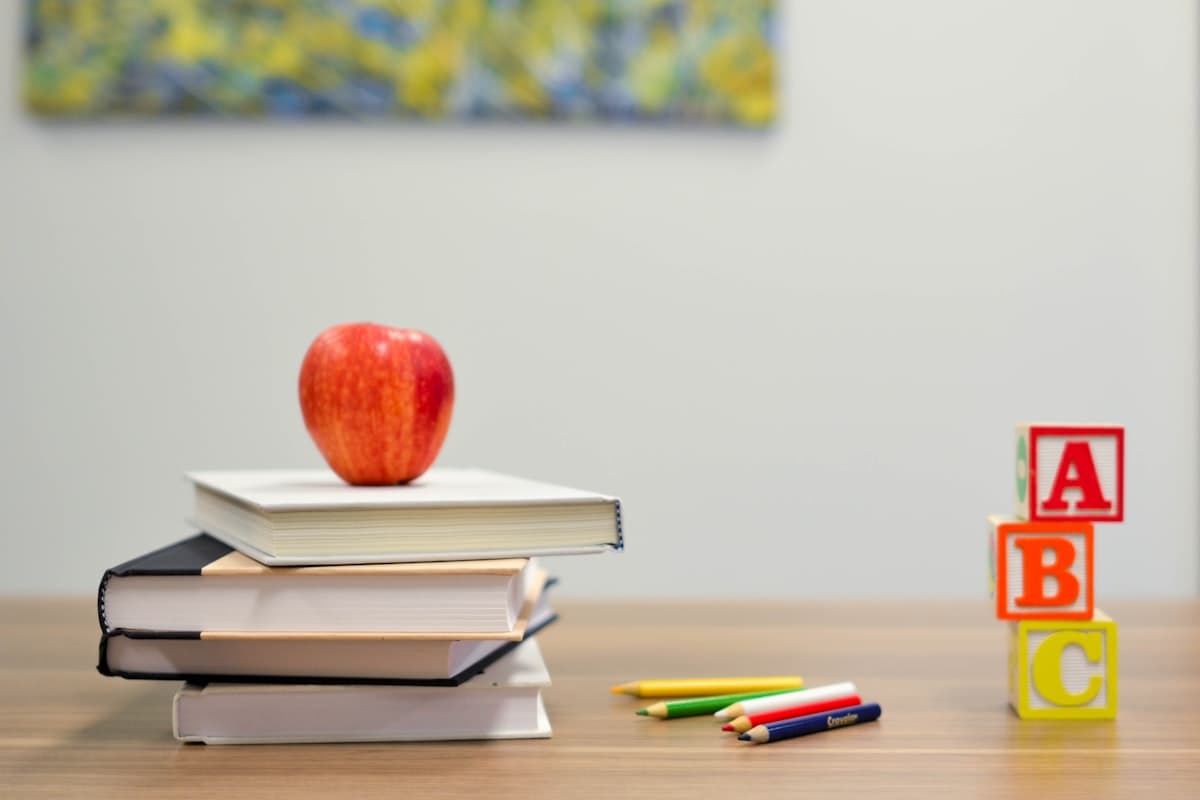 A stack of books with an apple on top, on a school desk