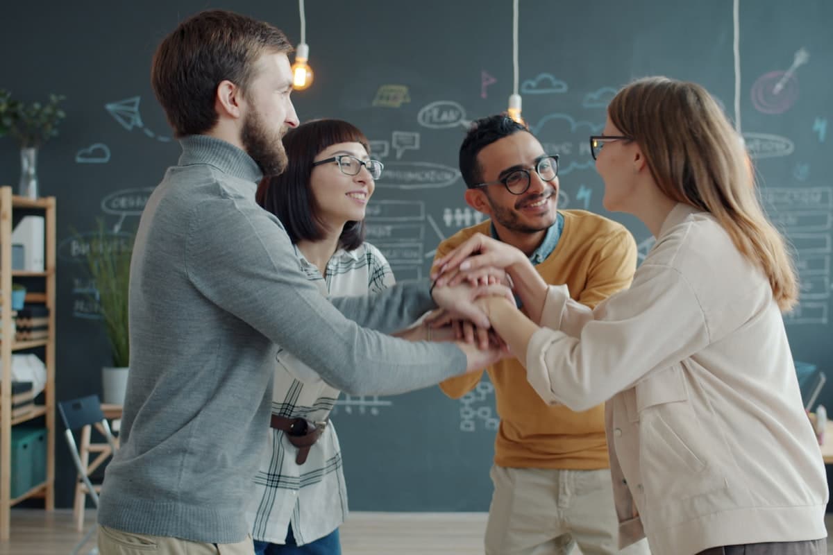 A team of colleagues putting their hands together in a huddle, welcoming a new team member