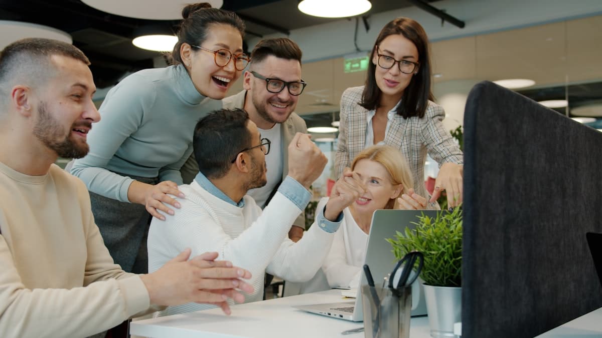 A team celebrating together around a laptop with cheers and raised fists
